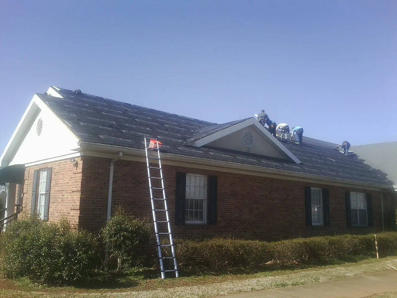 Crew tearing shingles off a brick ranch roof with a ladder set — Metal Roof Repair work by our crew in Shohola