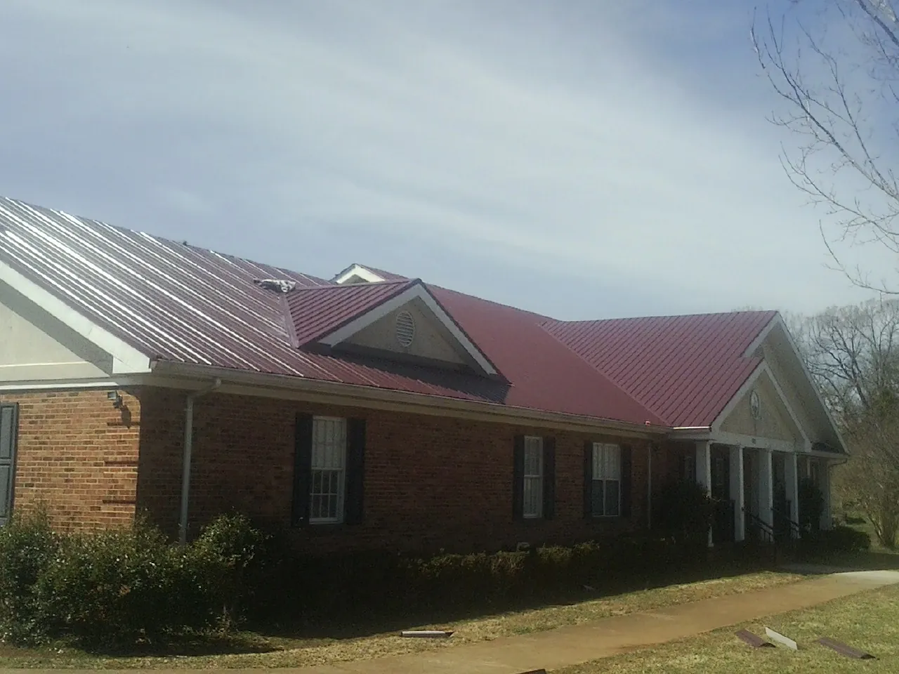 Red metal roof with gabled entries on a long brick building, from a Hail Damage Roof Repair job in Shohola