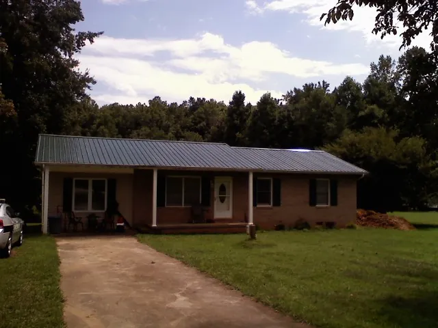 Dark green metal roof on a brick ranch with a covered porch in Shohola