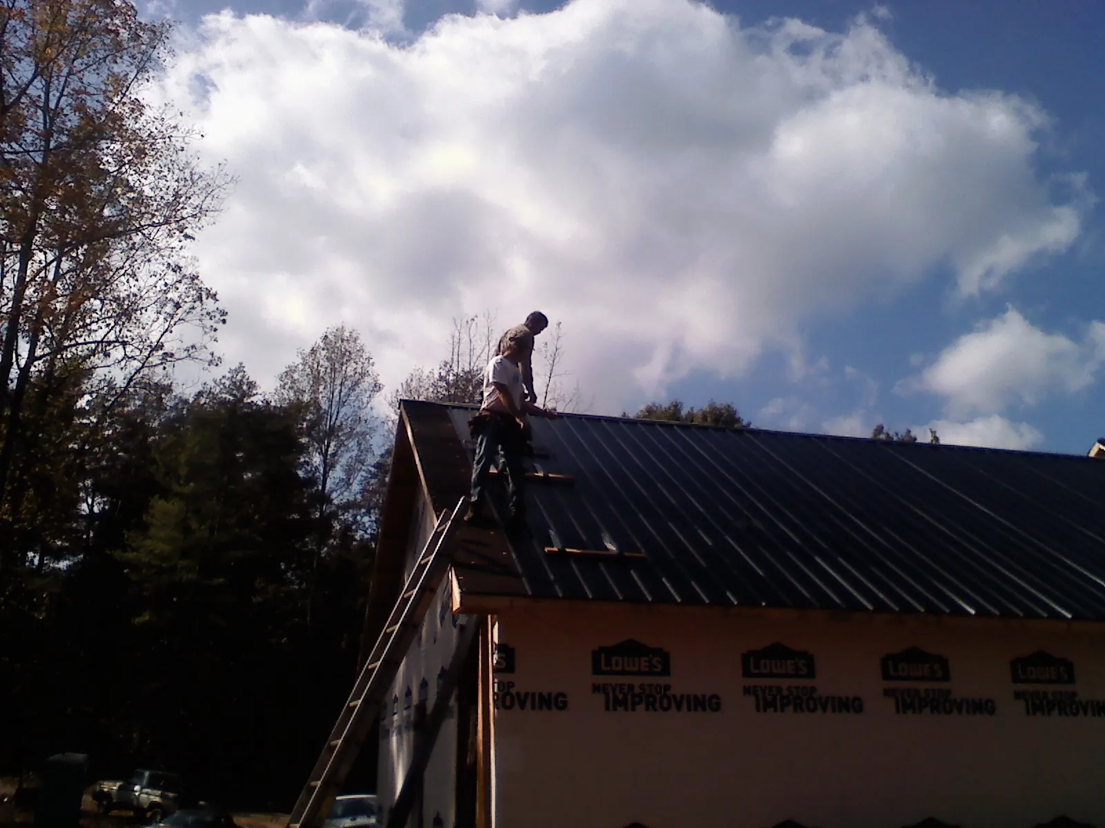 Roofer fastening dark metal panels high against a cloudy sky, from a Roof Inspection job in Shohola