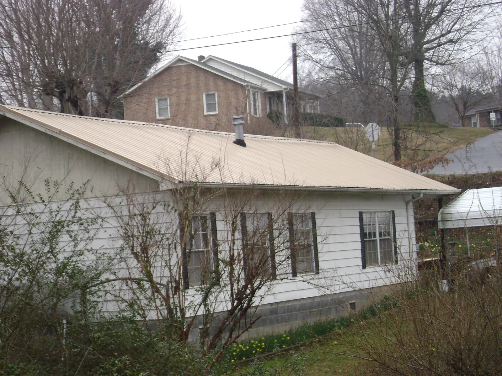 Tan metal roof on a white sided house set into a hillside — Commercial Roofing by Roofing Brothers in Shohola